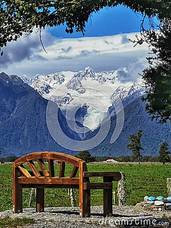 A view on the Fox Glacier on the South Island of New Zealand with a solid wooden seat on the foreground Stock Photo