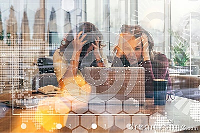 View through glass. Two business women are sitting in front of laptop, clutching their heads. Brainstorming, teamwork. Stock Photo