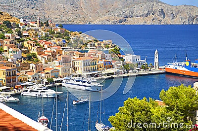 View on Greek sea Symi island harbor port, classical ship yachts, houses on island hills, tourists Aegean Sea bay. Greece islandsV Stock Photo