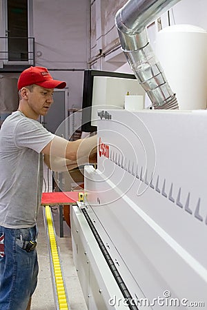 Industrial carpenter worker operating wood cutting machine during wooden door furniture manufacturing Editorial Stock Photo