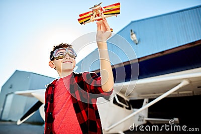 Happy kid playing with toy airplane near hangar, dreams to be a pilot Stock Photo