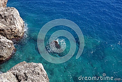 View from high rocky shore to the azure transparent sea water with foam in sunny day Stock Photo