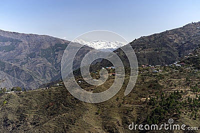 View of a Himalayan village on slop of mountain and snow capped mountain ranges Stock Photo