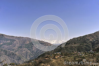 View of a Himalayan village on slop of mountain and snow capped mountain ranges Stock Photo