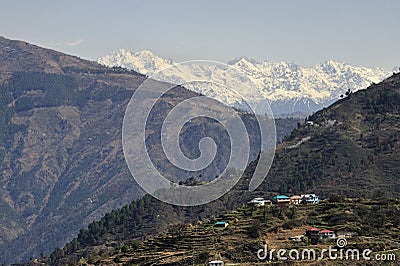 View of a Himalayan village on slop of mountain and snow capped mountain ranges Stock Photo