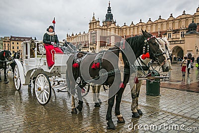 A view of a horse drawn carriage riding past the Adam Mickiewicz Monument and Cloth Hall in the medieval old town square in Krakow Editorial Stock Photo