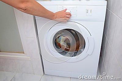 View on how a woman is turning on of the washing machine. A woman is choosing a washing mode on the washing machine Stock Photo