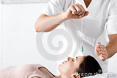 View of hypnotist standing near woman and holding green stone above her face Stock Photo