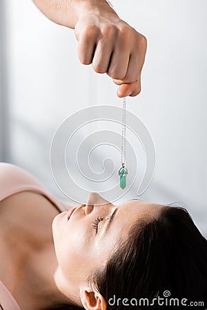 View of hypnotist standing near woman and holding green stone above her face Stock Photo