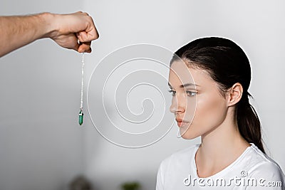 View of hypnotist standing near woman and holding green stone near her face Stock Photo