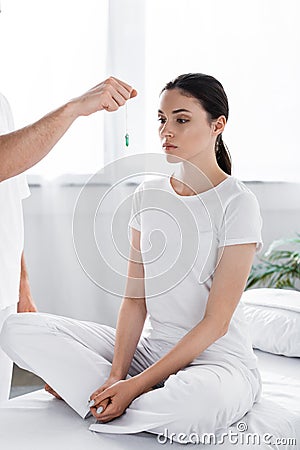 View of hypnotist standing near woman and holding green stone near her face Stock Photo