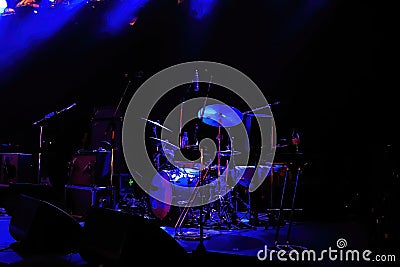 View on illuminated empty live stage with blue illuminated drum percussion kit and microphones focus on cymbal right of center Stock Photo