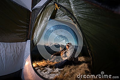 Two male tourists have a rest in the camping in the mountains at night under night sky full of stars and milky way Stock Photo