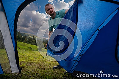 View from inside the tourist tent. Setting up a camp night. A man opens the entrance to a tent. Hiking and travel concept. Stock Photo