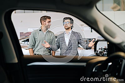 View from interior of car to professional car dealer selling new automobile to male client explaining characteristics Stock Photo