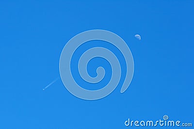 JET TRAILING CONTRAILS AND HALF A MOON IN THE BLUE SKY AT DAYTIME Stock Photo