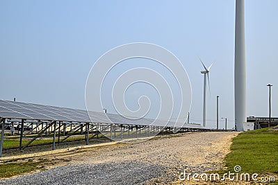 View of a long array of solar panels with an electric generating wind turbine in the background Stock Photo