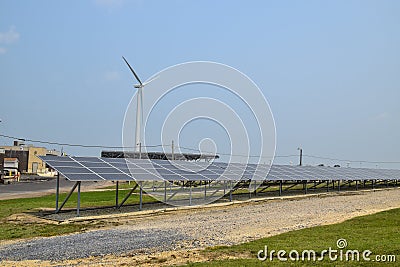 View of a long array of solar panels with an electric generating wind turbine in the background Stock Photo