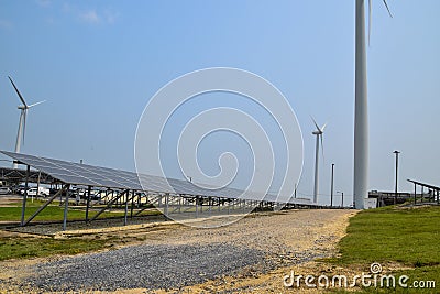 View of a long array of solar panels with two electric generating wind turbines in the background Stock Photo