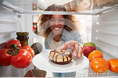 View Looking Out From Inside Of Refrigerator As Woman Opens Door And Reaches For Unhealthy Donut Stock Photo