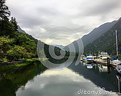 A view of a marina full of boats on a rainy grey day in at the end of remote, secluded inlet surrounded by forests and mountains. Stock Photo