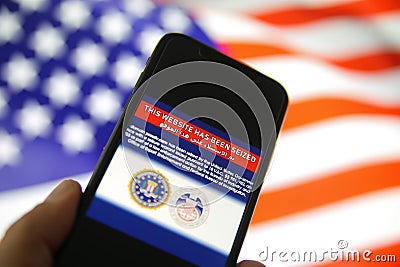 View on mobile phone screen with FBI notification this website has been seized, blurred us flag background Editorial Stock Photo