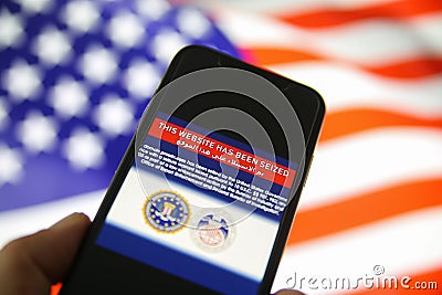 View on mobile phone screen with FBI notification this website has been seized, blurred us flag background Editorial Stock Photo