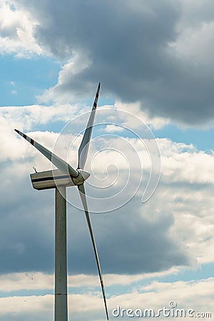 view of a modern windmill against a blue sky. The white blades of the wind turbine close up. Renewable energy source. Production Stock Photo