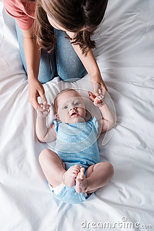 View of mother in denim jeans sitting near adorable infant in blue baby bodysuit Stock Photo