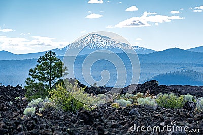 View of Mt. Bachelor from Newberry Volcano National Monument. Black lava rocks, trees and desert vegetation in foreground Stock Photo