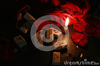 View of the mystical composition of wooden runes around the petals of red roses, a candle burns next to it and the burnt matches Stock Photo