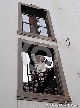 a view of an old factory chimney through the window of an abandoned destroyed industrial building with twisted burned metal Stock Photo