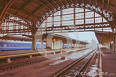 View of the old railway station with a large metal arch and an empty platform with a clock Stock Photo