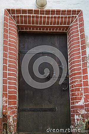 View of the old wooden door, forged metal hinges, locks, beautiful decorative finish outside with brick. Architecture, elements Stock Photo