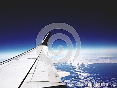 Airplane wing over cloudy earth surface with dark blue horizon Stock Photo
