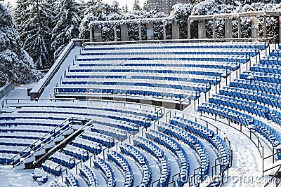 View of outdoor amphitheater rows of blue plastic seats covered in snow at winter time on sunny day Stock Photo