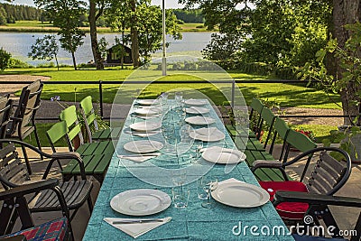 View of outdoor party table covered with sea green table cloth ready served. Beautiful nature around. Stock Photo