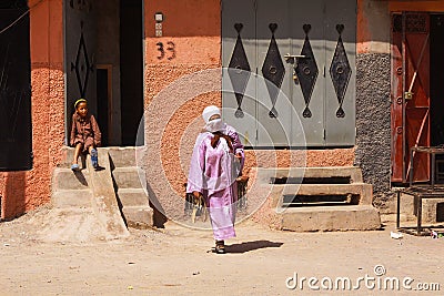 View over dirt square on oriental style house front entrance with one boy sitting on steps and muslim veiled woman with pink tunic Editorial Stock Photo