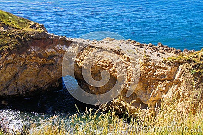 View over grass on natural sandstone bridge with arch in the ocean Stock Photo