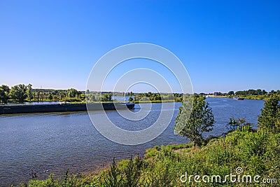View over green rural landscape on river Maas with inland waterway vessel against blue summer sky - Between Roermond and Venlo, Stock Photo