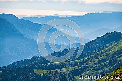 View over the Green Valley, surrounded by high mountains on a summer sunset. Layers of mountains in the haze during sunset Stock Photo