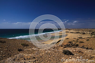 View over sand dunes with green ocean on Playa del Aljibe on white village on steep cliff El Cotillo - North Fuerteventura Stock Photo