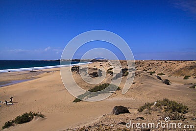 View over sand dunes with green ocean on Playa del Aljibe on white village on steep cliff El Cotillo - North Fuerteventura Stock Photo