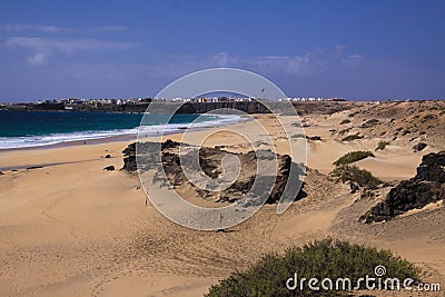 View over sand dunes with green ocean on Playa del Aljibe on white village on steep cliff El Cotillo - North Fuerteventura Stock Photo