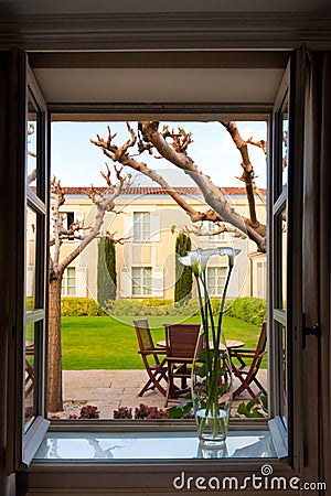 View out of opened window with vase on sill to backyard with patio, formal garden of Chateau Cordeillan-Bages, Bordeaux, France. Stock Photo