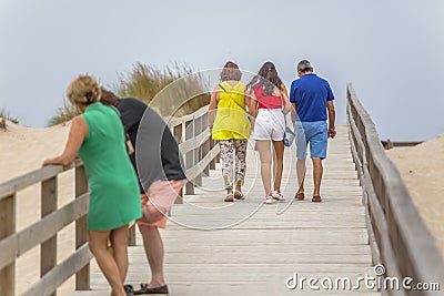 View of pedestrian path on beach, backs of couple with daughter walking on wooden path and other couple talking Editorial Stock Photo