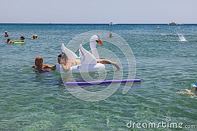 View of people swimming in sea. Couple on inflatable white swan on front. Rhodes. Editorial Stock Photo