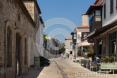 View of people walking on street and old, historical, traditional stone houses in famous, touristic Aegean town called Alacati. Editorial Stock Photo