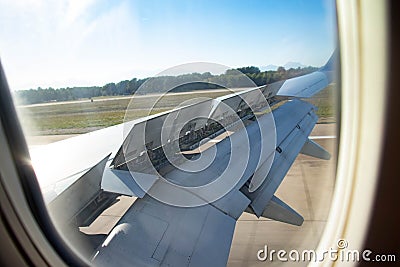 View from the porthole of an airplane wing taking off over the runway at high speed during sunset. The ground passes under the Stock Photo