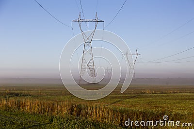 View of power line towers in fields during a beautiful misty late summer golden hour morning Stock Photo